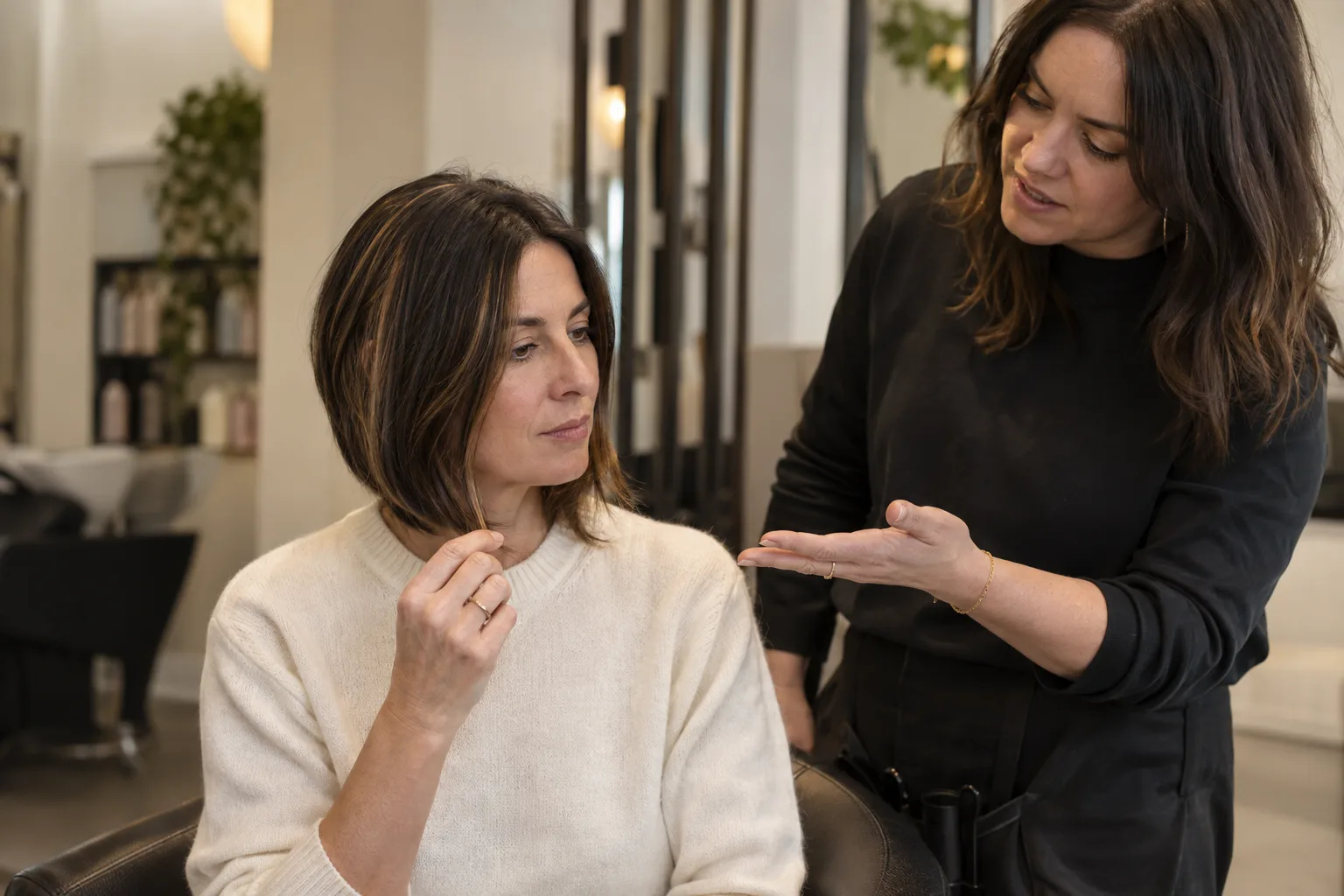 Woman comparing autumn bob haircuts with a stylist, holding her highlighted brunette hair at chin level